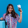 beautiful tourist woman holding travel suitcase passport with tickets with smile face happy positive travel concept standing blue space